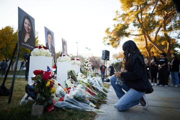woman holding flowers in front of three photos during memorial vigil