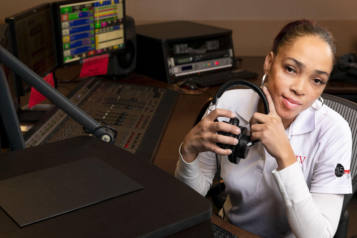 A woman inside of a radio studio, holding a pair of headphones.