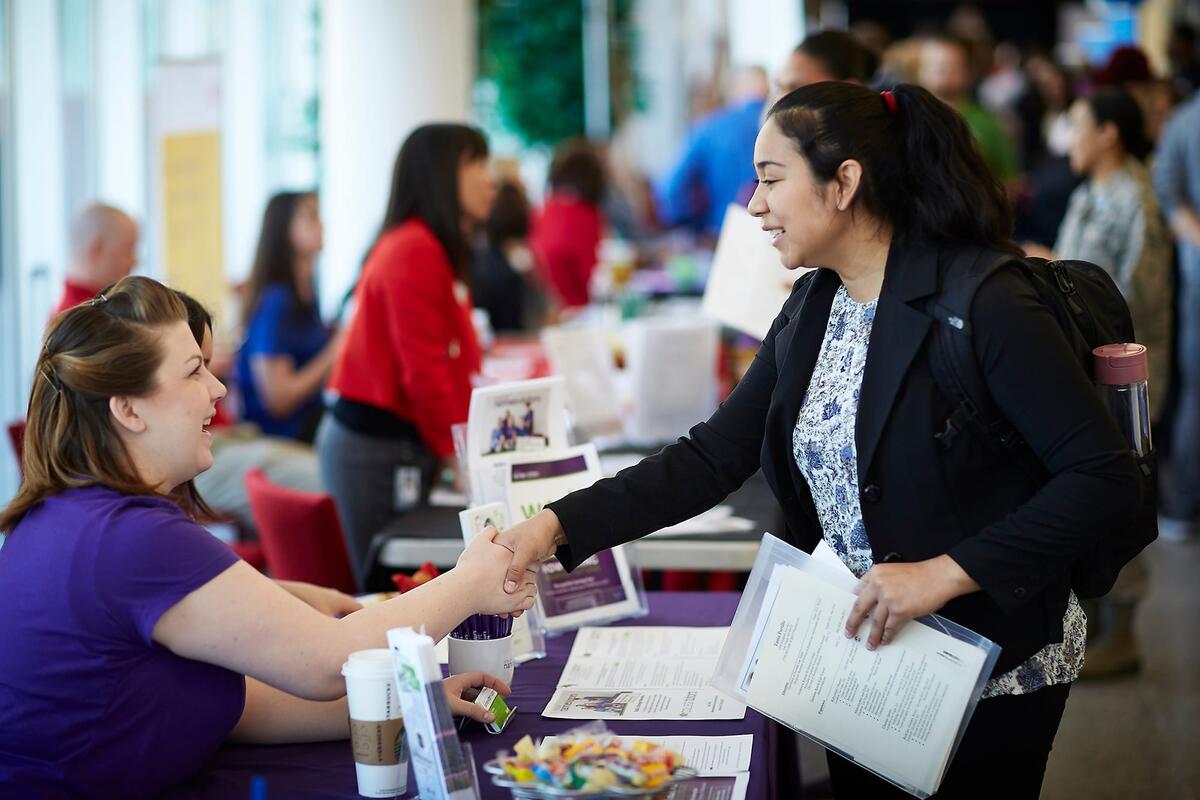 Student at a career fair shaking hands with a representative at a booth