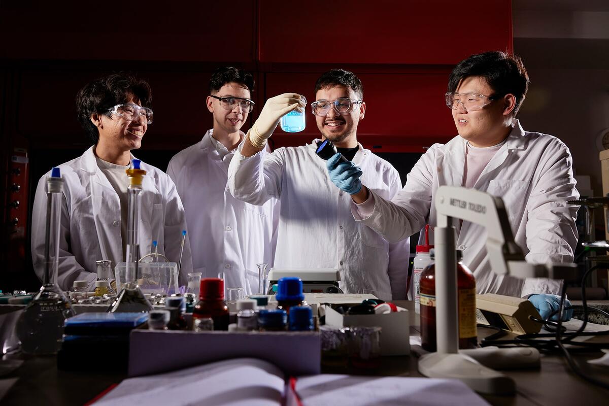 A group of research students with one student shining a black light through a beaker of liquid