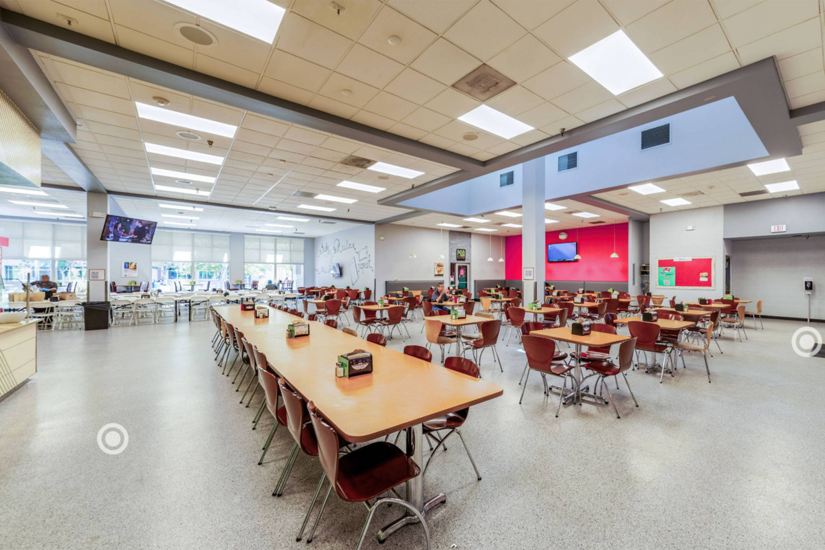 A large scale view of the area across from he GRAZE deli and salad bar. Square tables with four chairs are spread about the area as well as longer tables with an abundance of chairs.