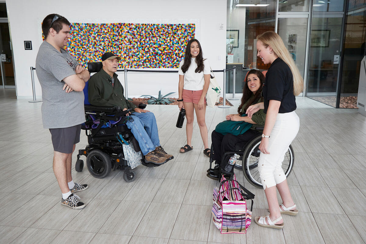 Group of five people speaking together, two are in wheelchairs and three are standing