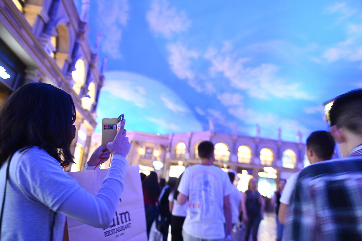 People taking pictures of an indoor ceiling painted like the sky
