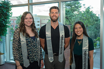 Three students wearing gray ambassador sashes