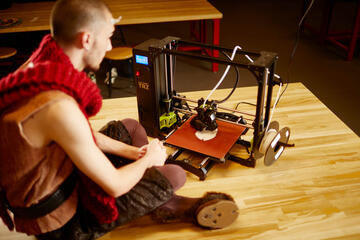 A man in costume looks at a 3D printer