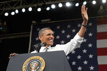 Bottom view of President Obama standing at a podium while he smiles and waves to his left.