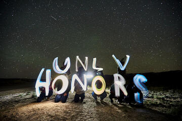 Group at night lighting up "UNLV HONORS" letters with flashlights.