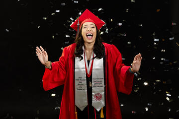 Woman in a red graduation cap and gown with confetti