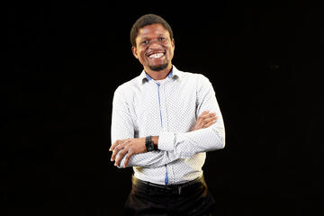 smiling man with folded arms wearing button-down shirt stands in front of a black background