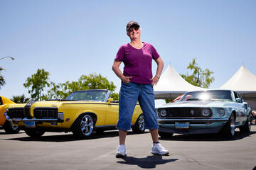 woman strongly poses in front of two classic Mustang cars
