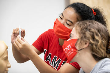 U.N.L.V. nursing student in red shirt reviewing slide sample with peer