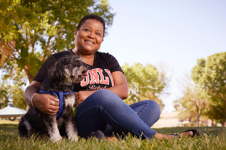 Michele Washington, Claims Administration Coordinator for Risk Management &amp; Safety with Aries, her Maltese Poodle mix in a park.