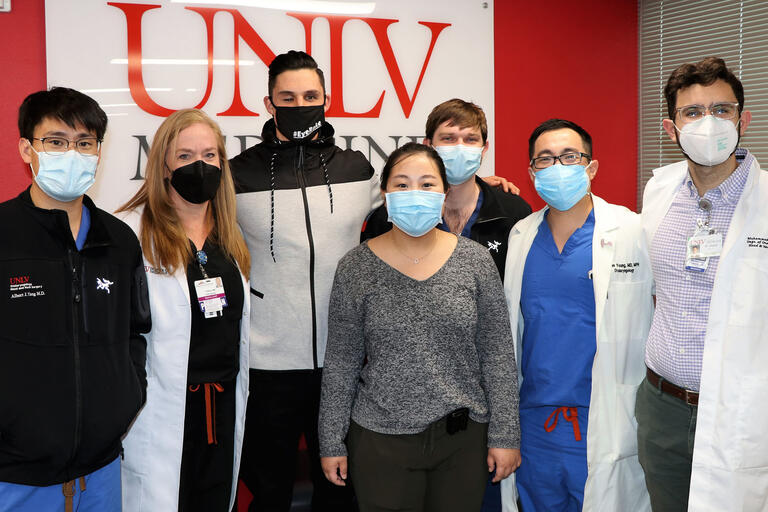 A group of doctors and a patient stand in front of a UNLV Medicine sign