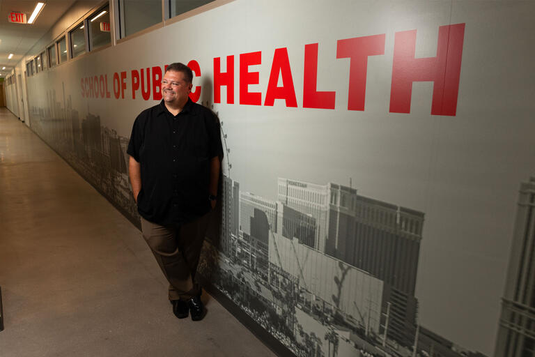 A man stands in front of a wall that reads &quot;School of Public health&quot;