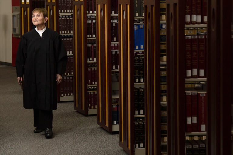 A woman in judge's robes walks through the stacks of a law library