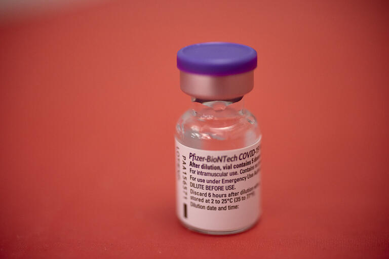 Pfizer vaccine vial against a red background