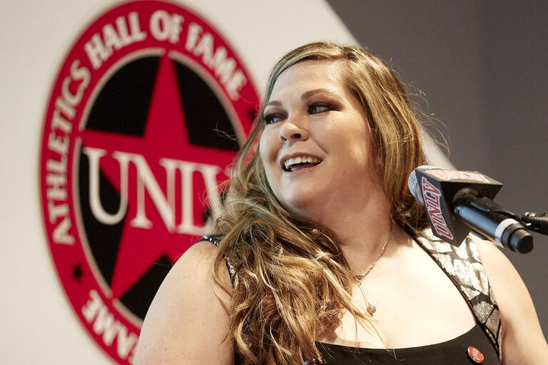 woman at podium with &quot;UNLV Athletics Hall of Fame&quot; logo in background