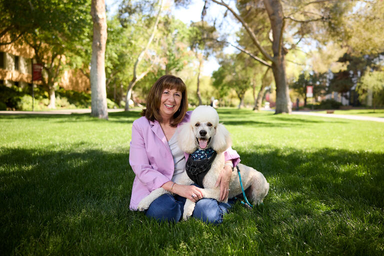 woman sitting with her standard toy poodle on the grass