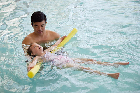 A swim instructor helping a child to swim on pool noodles