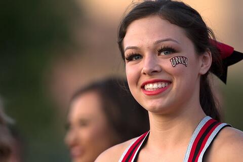 A smiling cheerleader with U-N-L-V painted on her cheek.