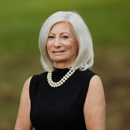 A smiling woman with blonde hair wearing a black turtleneck and blouse.