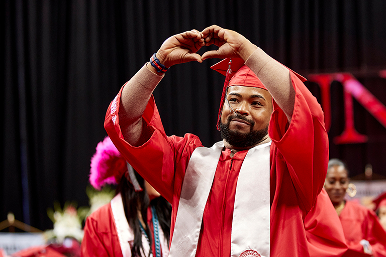 Granduate at commencement makes heart symbol with hands