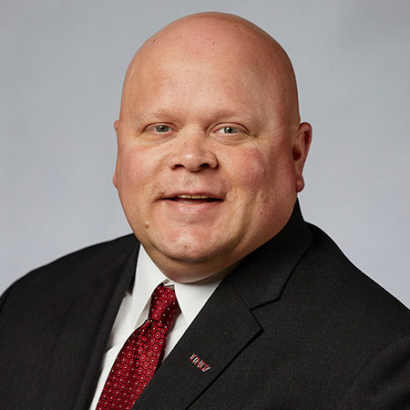 A bald man in a black suit and red dotted tie.