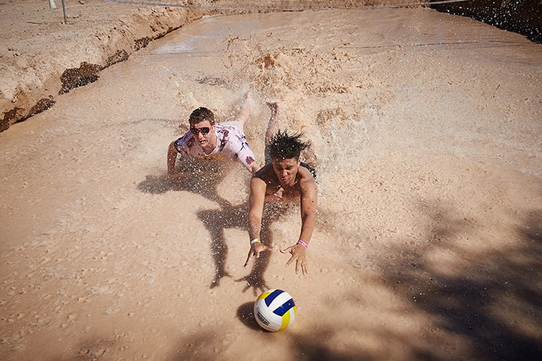 Two students chase after volleyball in muddy water