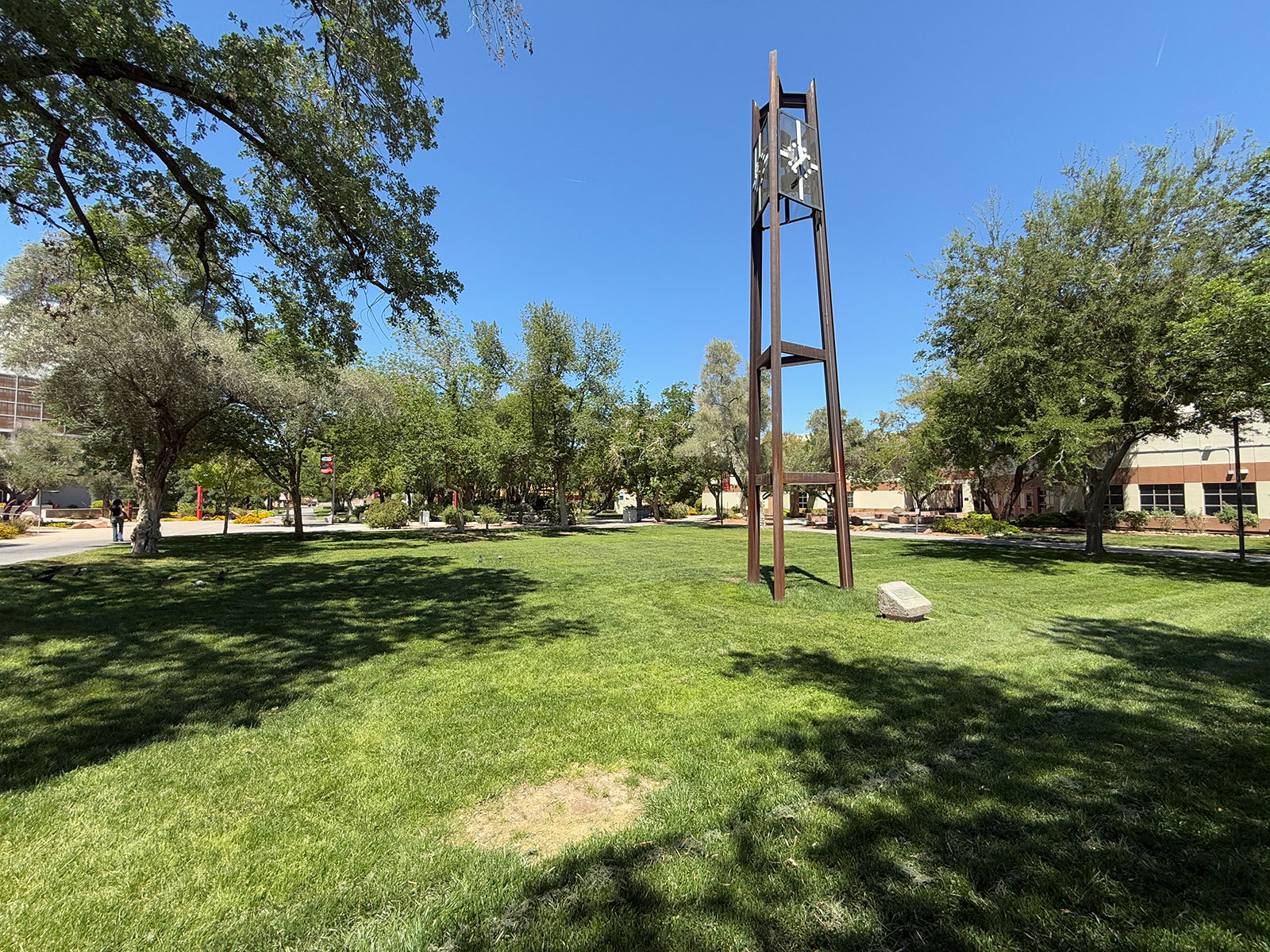 A grass field with trees on campus with a clock tower in the middle
