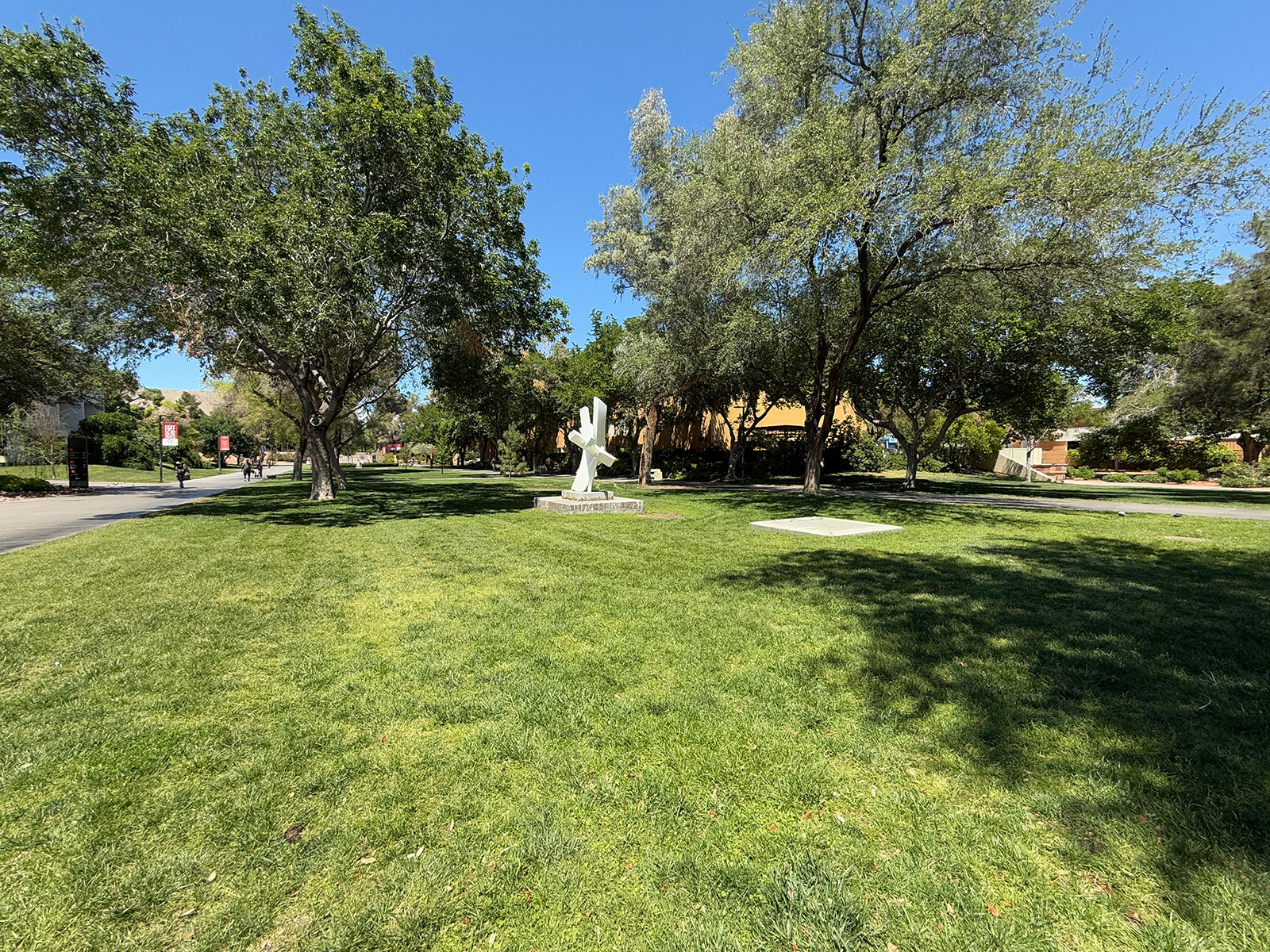 A grass field with trees on campus and the metal sculpture in the middle of it