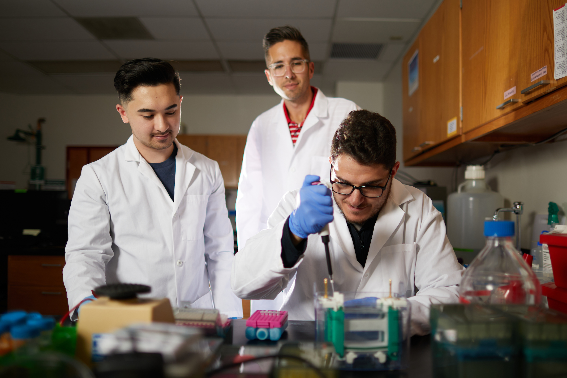 Student and professor observing another student with a pipette.
