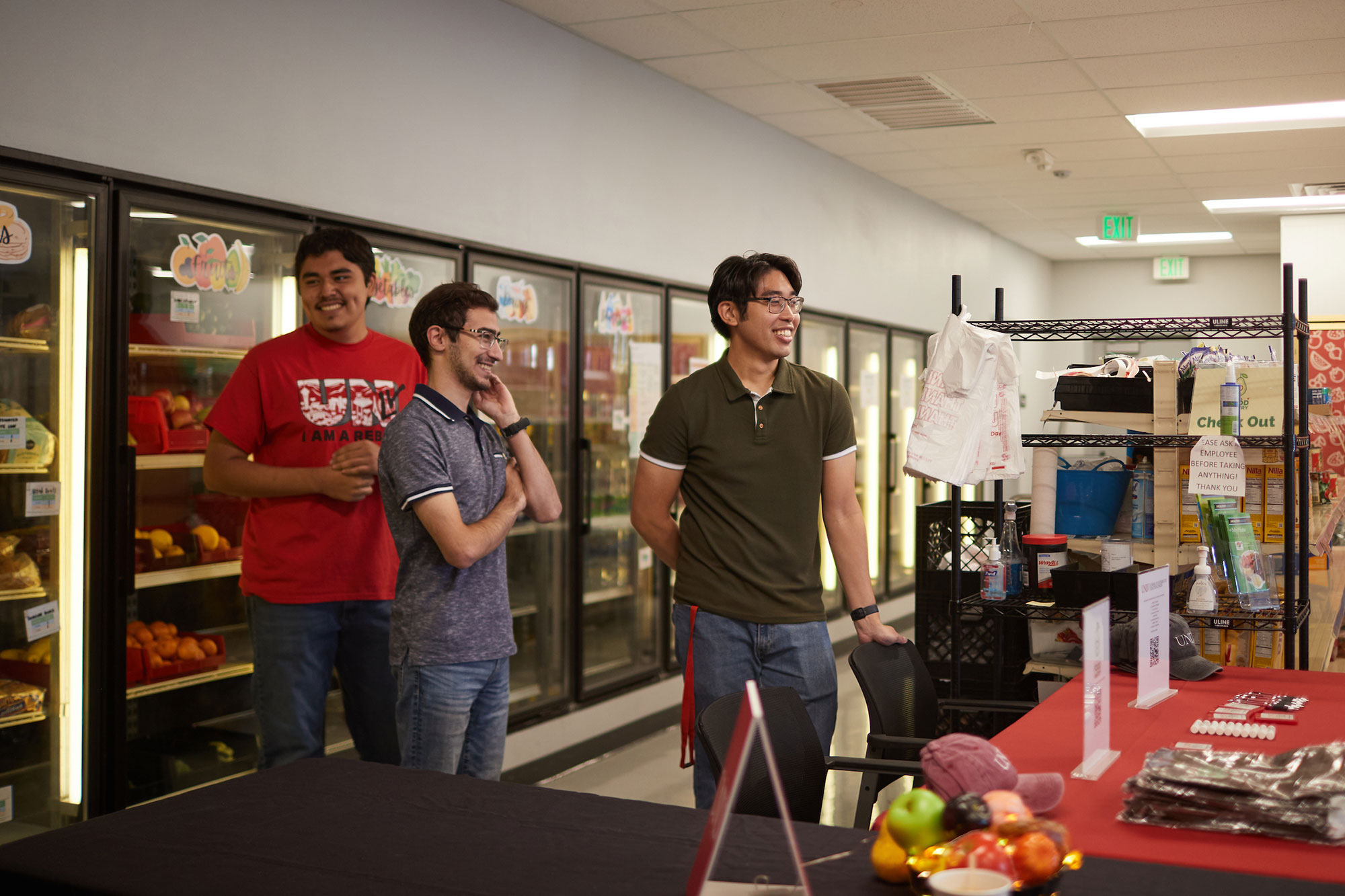 Three students standing in a food pantry, laughing and chatting.