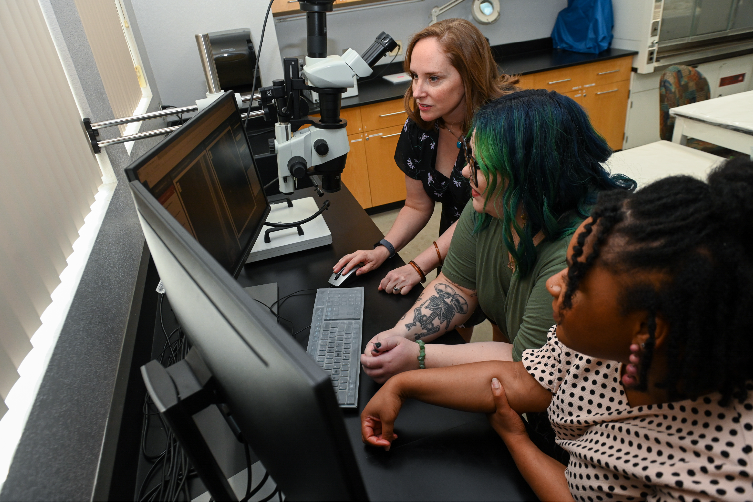 A professor seated by a computer with two student
