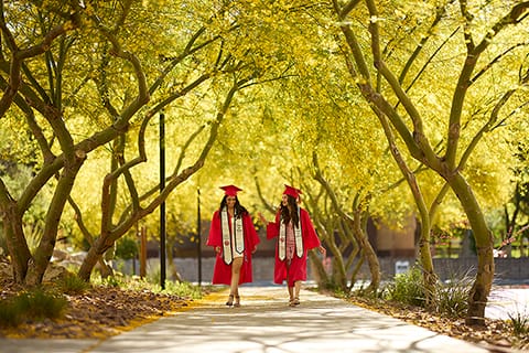 LiedTwo students in cap and gown pose under trees