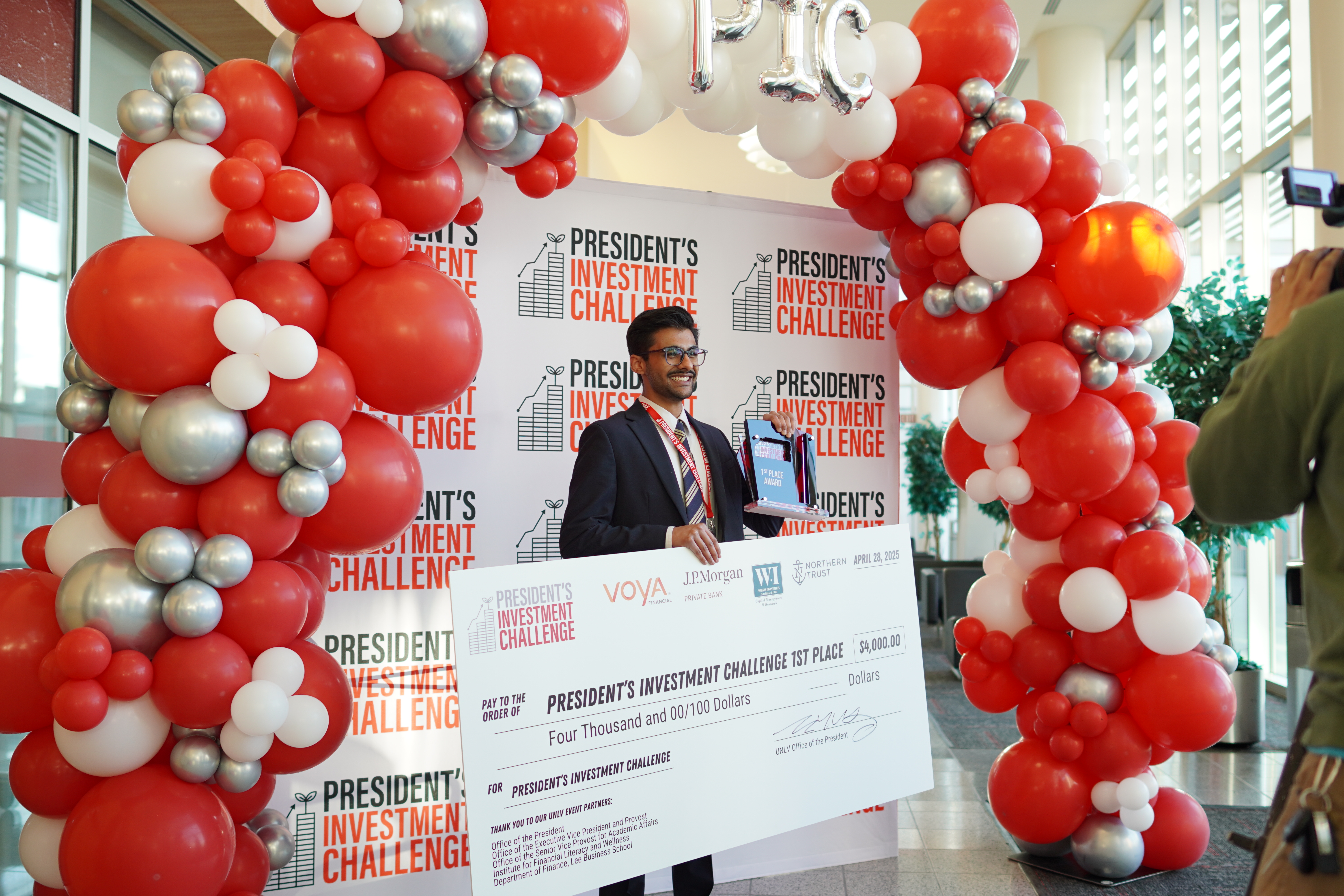 A person in front of a backdrop taking photos with a large check and a 1st place award for the President's Investment Challenge