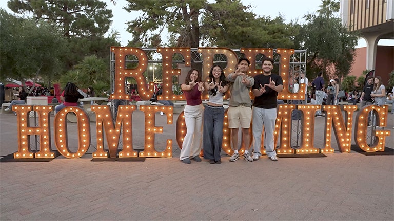 Students stand in front of a Homecoming sign