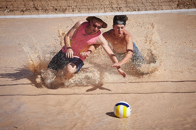 two people race towards volleyball in muddy water