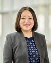 portrait of Yvonne Chen, wearing gray blazer, navy patterned top, and smiling