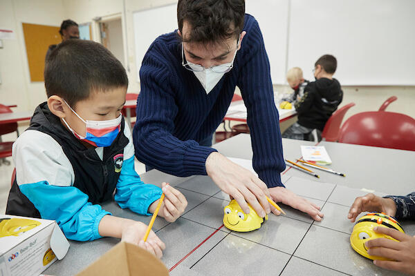 Graduate student working showing elementary school students how to use a bee-shaped robot
