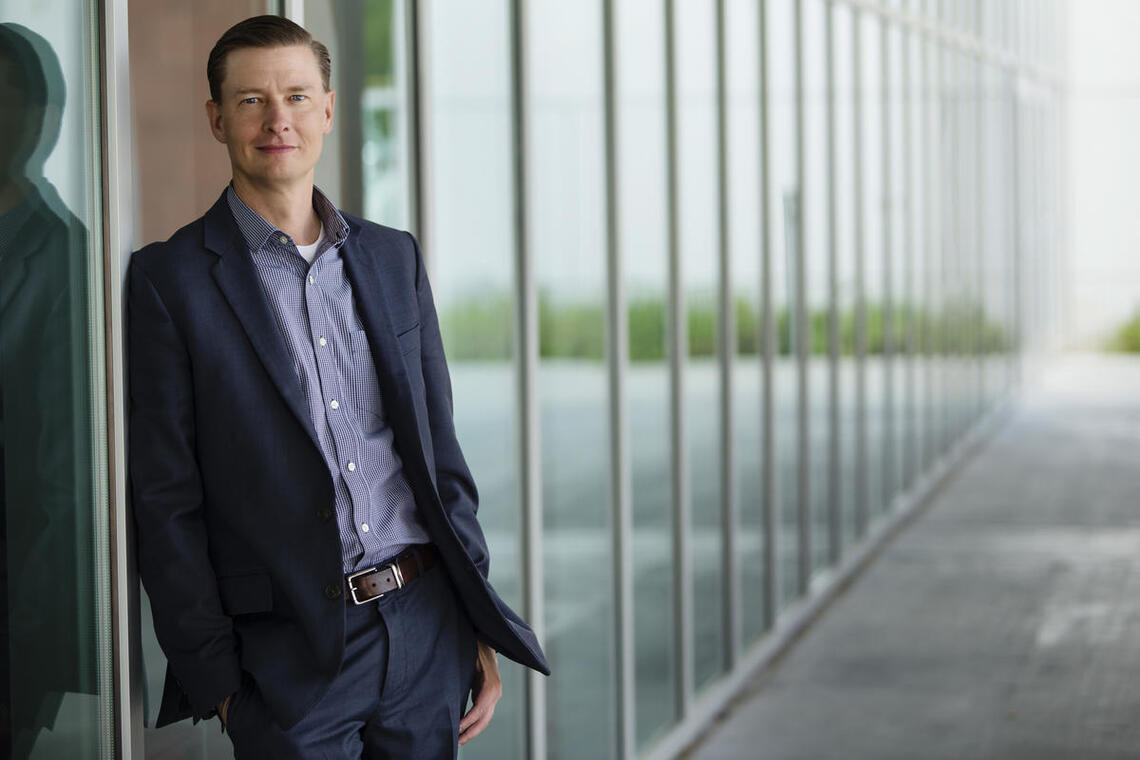 A smiling man leaning against a building wall.
