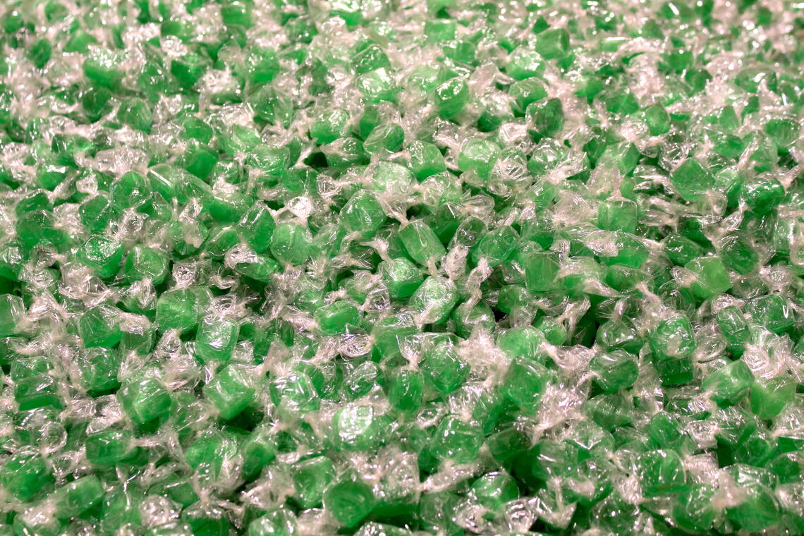 A pile of small, square, green hard candies wrapped in clear cellophane.