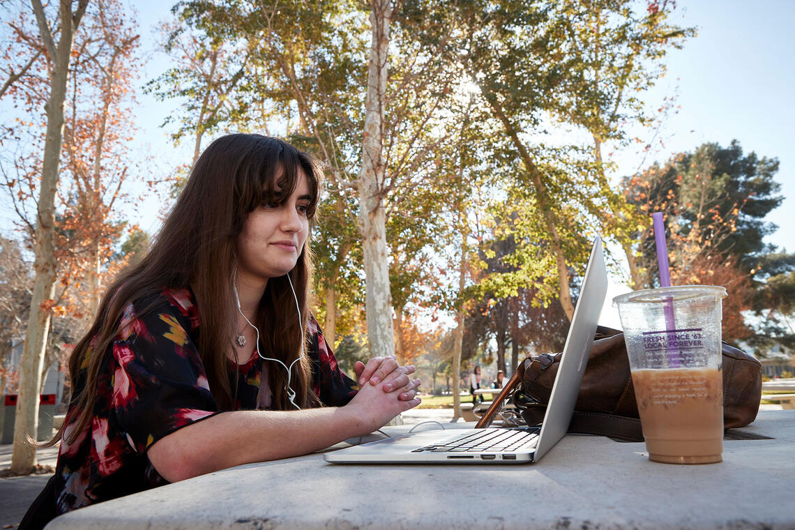 A woman sitting down at a table with a laptop and coffee