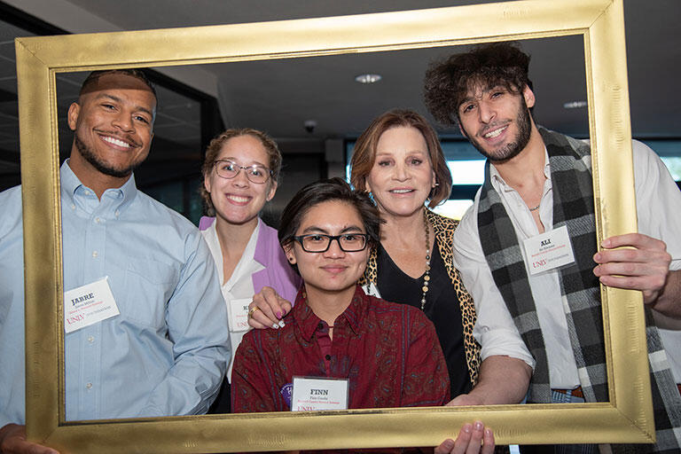 Five people posing in front of a golden frame.