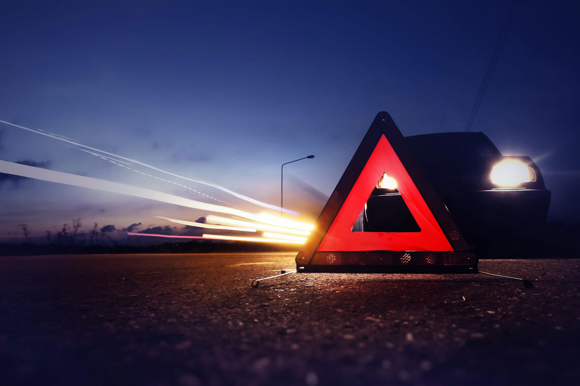 Red emergency triangle warning sign with long-exposure of traffic light trails at night.