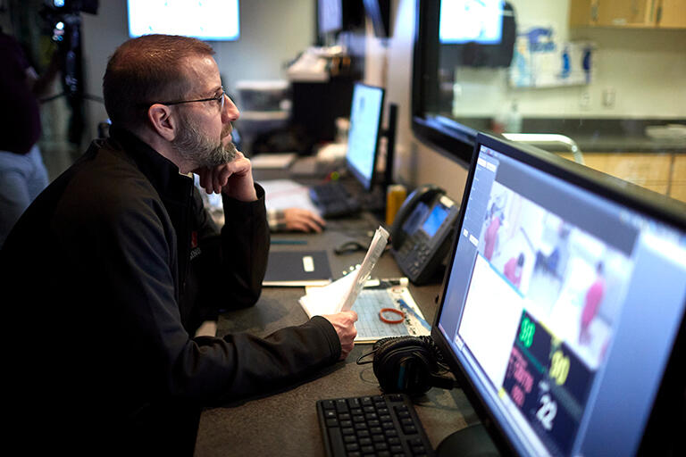 Man looking through a computer that screens viewing the simulation center.