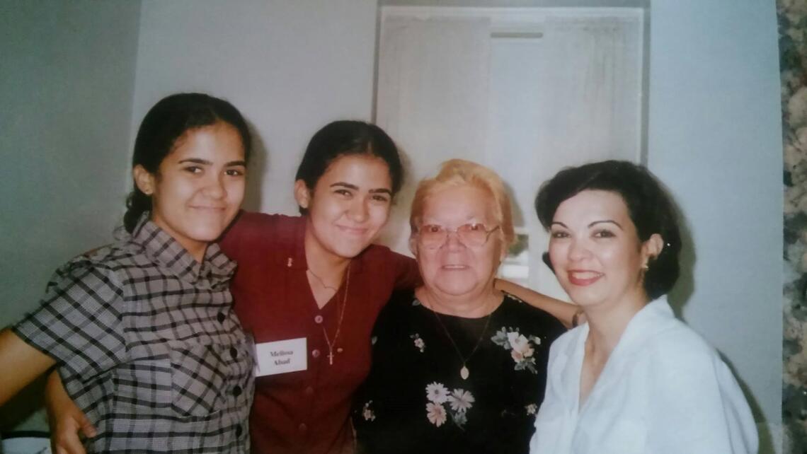 A group of women of 3 different generations smiling at the camera with their arms around each other