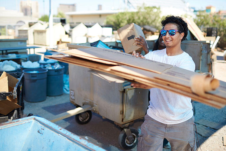 A man recycling cardboard into a recycle bin.