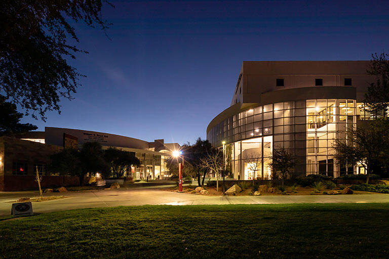 A view of large building and infrastructure built on campus, lit up with lights in the evening.