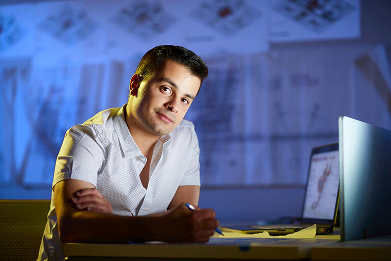 Un hombre joven trabajando en un escritorio con papeles y una computadora portátil abierta.