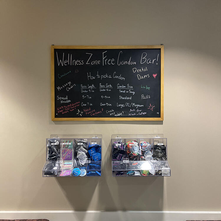 A chalkboard that says "Condom Bar." Below are storage cases of condoms